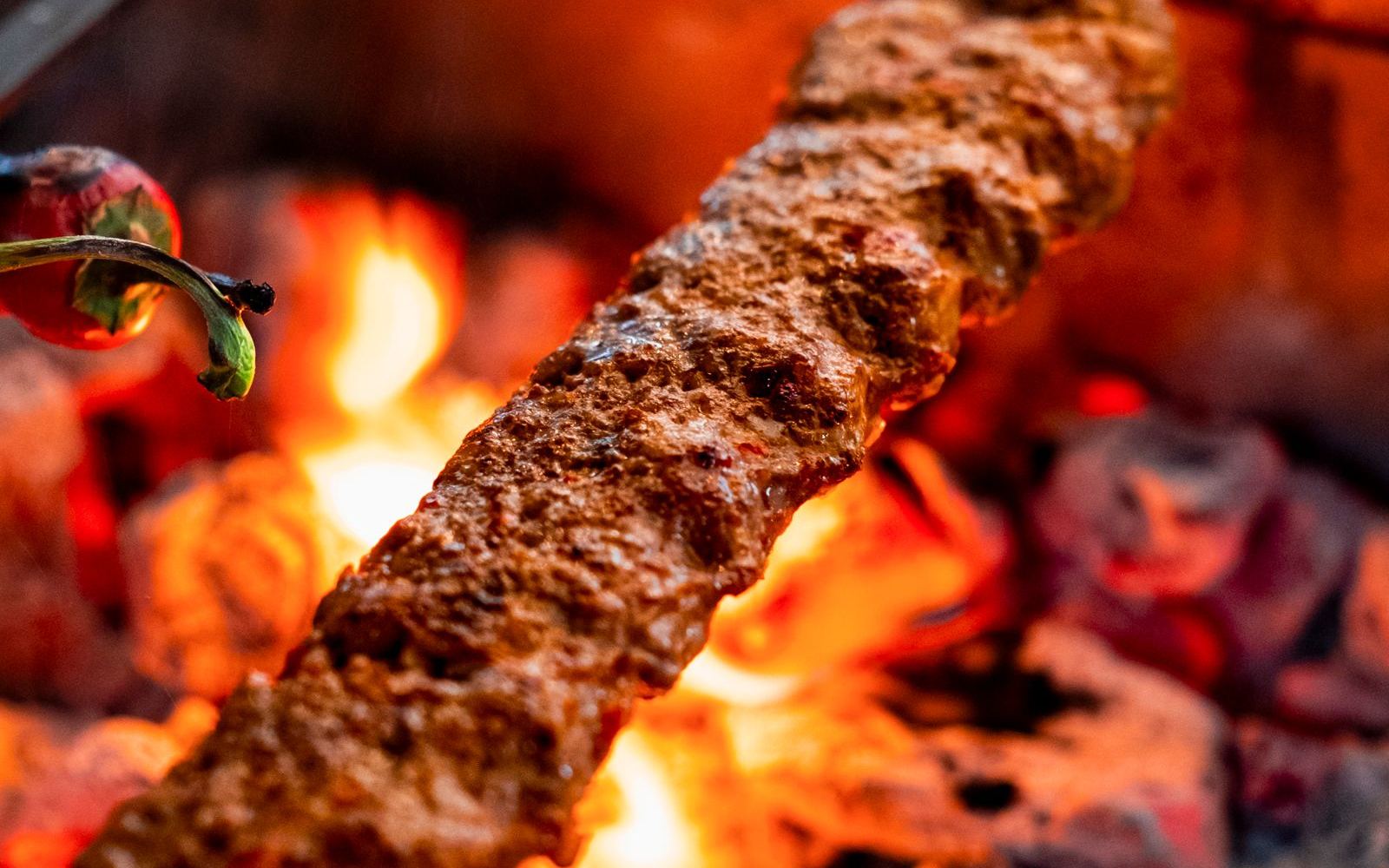 A spiced Adana kebab skewer grilling over charcoal flames